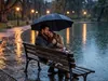 Romantic couple sitting in the rain, in the park